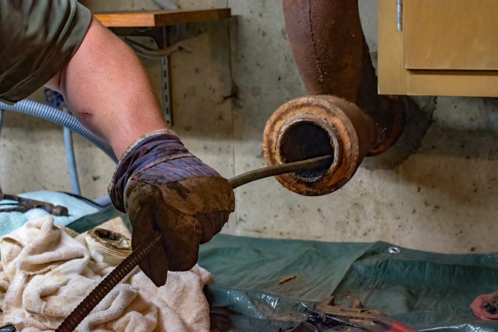 Hands of a plumber as he runs a camera scope and cleaning machine through the main pipe to unclog the drain to the Septic System. Hard-working tradesman.